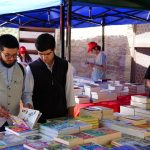 Pessoas consultam livros em uma feira literária ao ar livre.