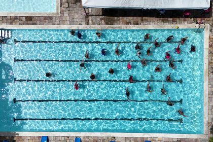 Vista aérea de pessoas nadando em raias de uma piscina pública.