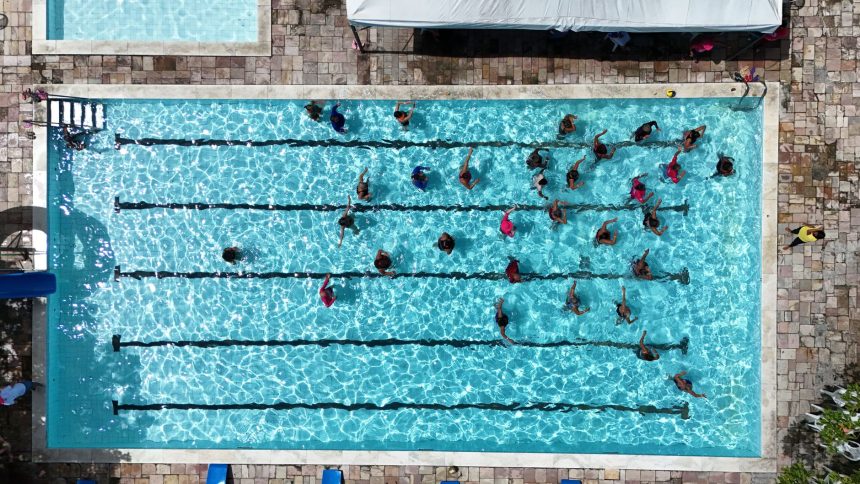 Vista aérea de pessoas nadando em raias de uma piscina pública.