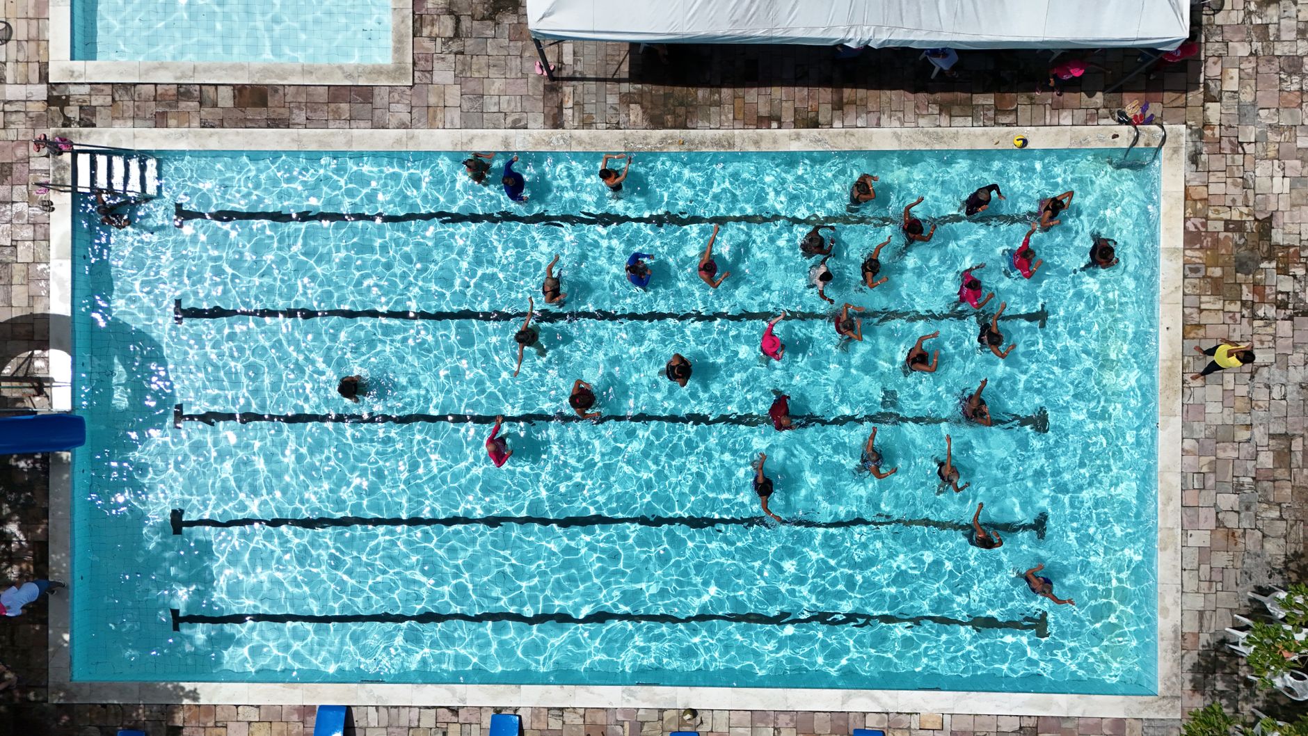 Vista aérea de pessoas nadando em raias de uma piscina pública.