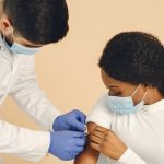 Profissional de saúde aplica uma vacina no braço de uma mulher em uma clínica.