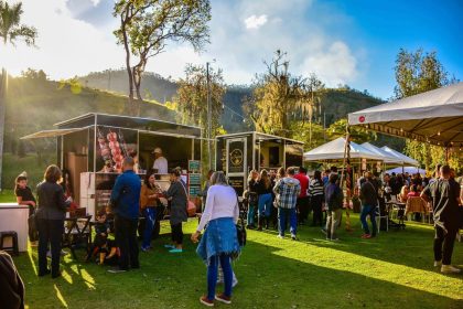 Público circula entre barracas de comida em um festival ao ar livre realizado em um parque brasileiro.