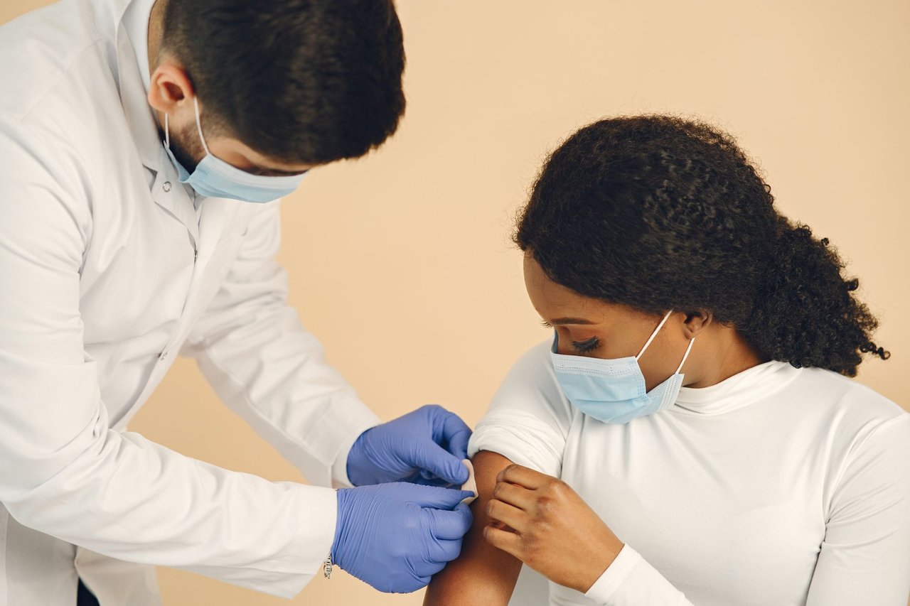 Profissional de saúde aplica uma vacina no braço de uma mulher em uma clínica.